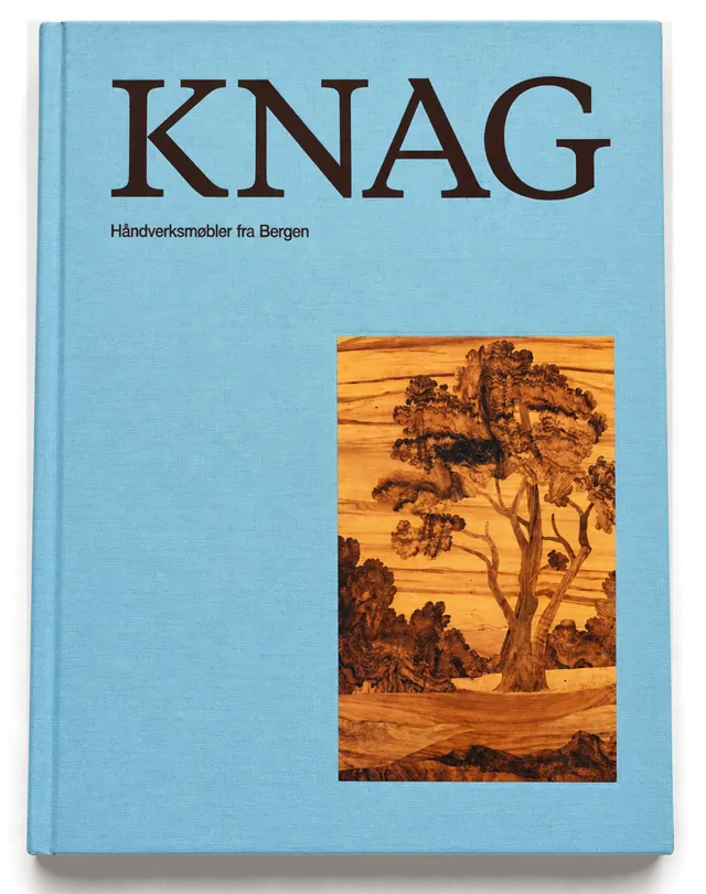 Omslaget til boken Knag – håndverksmøbler fra Bergen: lyseblått bind med tittelen i mørk skrift og et intarsiabilde av et tre